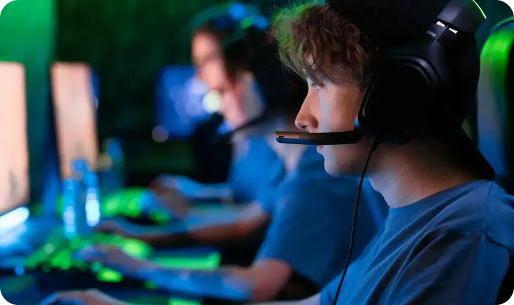 Een tienergamer met een headset op, geconcentreerd op een competitieve esports-wedstrijd, die samen met zijn teamgenoten op een pc speelt in een kleurrijke, met neon verlichte gamingopstelling.